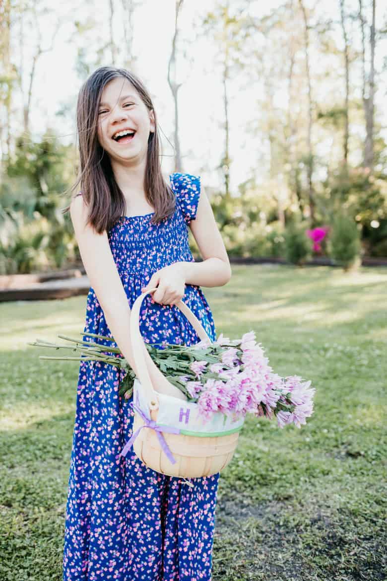 A young girl holds an easter basket with flowers wearing a long flowing kids easter outfits dress. 