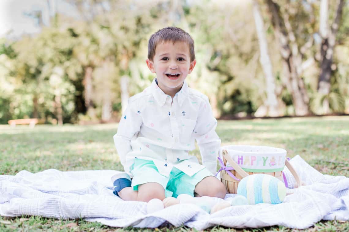 Toddler boy sits on a blanket with his easter basket wearing kids easter outfits