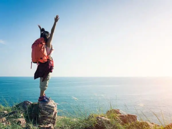 girl with arms up wearing backpack view of ocean